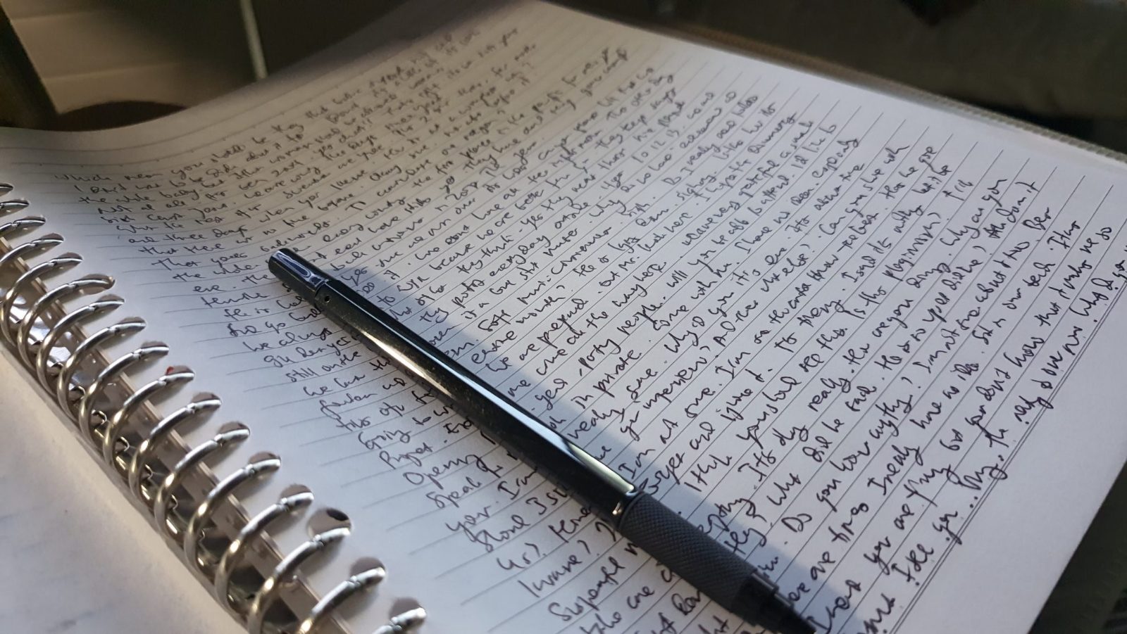 Un cuaderno de espiral escrito a mano, con un boligrafo encima.