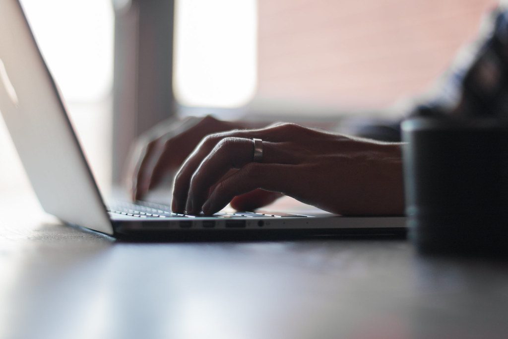 Unas manos escribiendo en el teclado de un portatil, con luz suave.