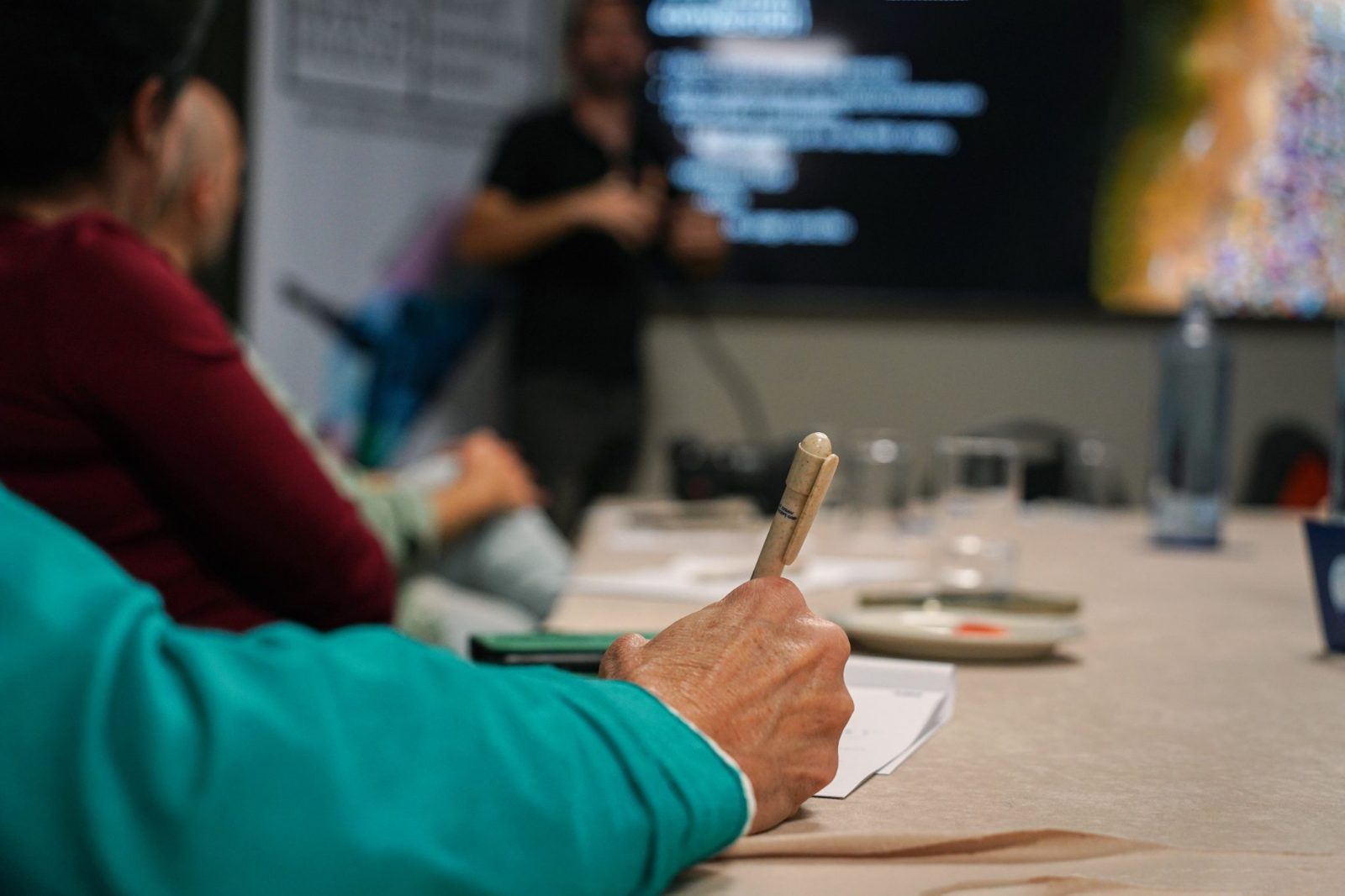 Una persona toma notas a mano en una mesa, durante una charla.
